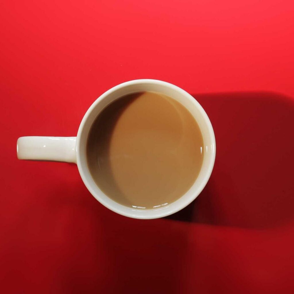 A white mug of milky coffee on a red background, seen from above