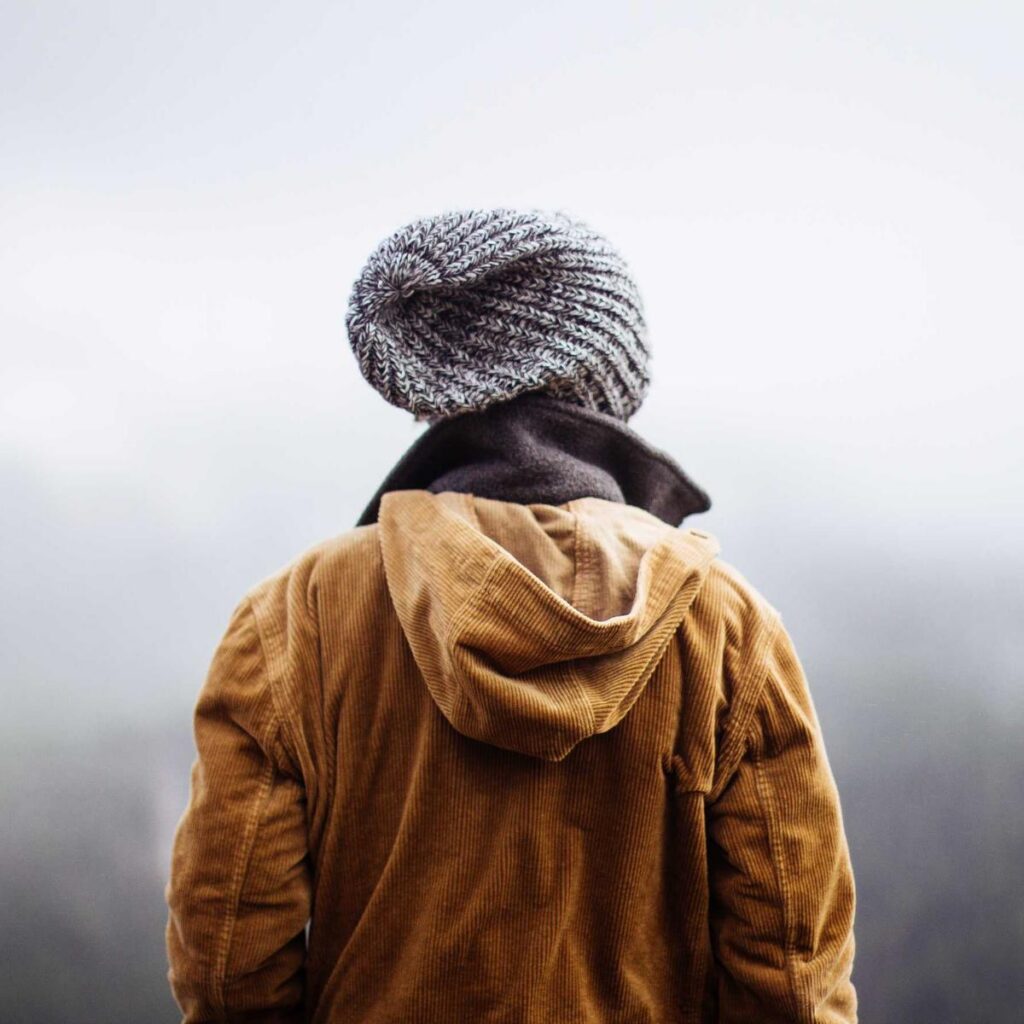 A walker in a tan waxed jacket and grey knitted beanie, seen from behind