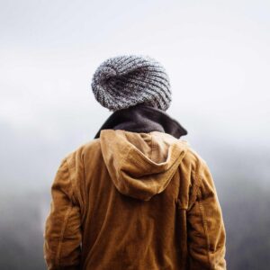 A walker in a tan waxed jacket and grey knitted beanie, seen from behind